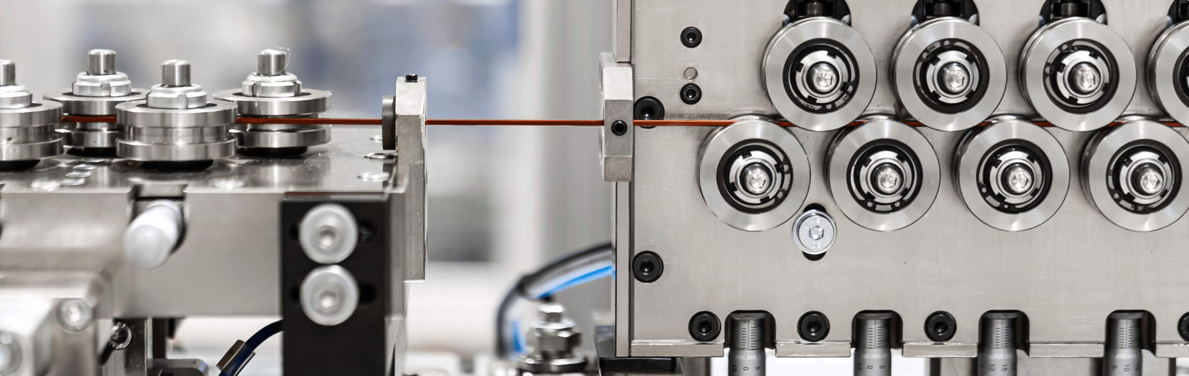Precision machinery at a VREMT facility used for manufacturing components of electric drives and batteries. The image shows a complex array of metallic rollers and guides processing a thin copper wire, indicative of VREMT’s innovative approach in enhancing electric vehicle technology